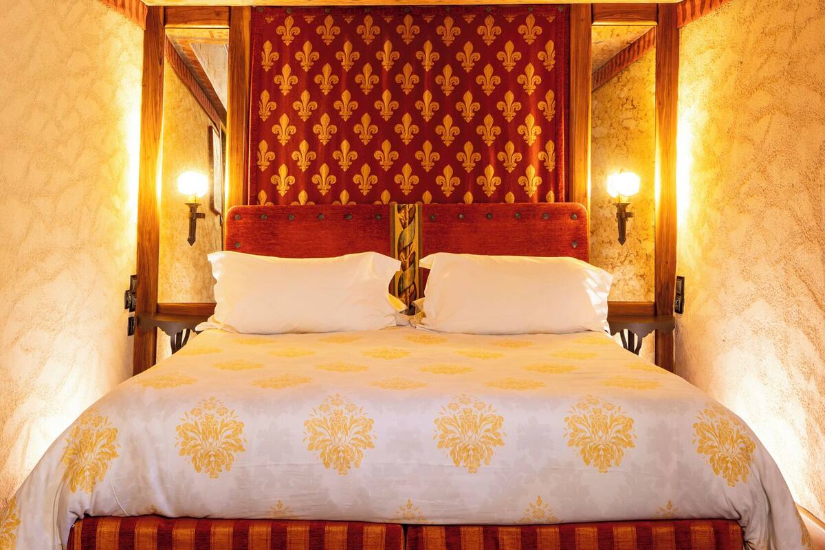 Una cama grande con cabecera roja y dorada, dos lámparas de noche y un techo decorativo.