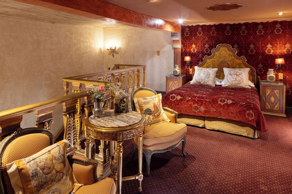 Un dormitorio lujoso con una cama grande, muebles ornamentados y una escalera decorativa.