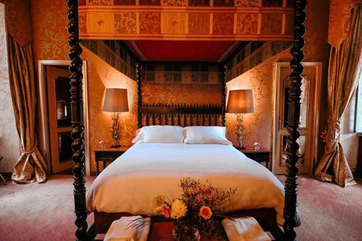 Una cama con dosel, dos mesitas de noche con lámparas y un arreglo floral sobre la cama.