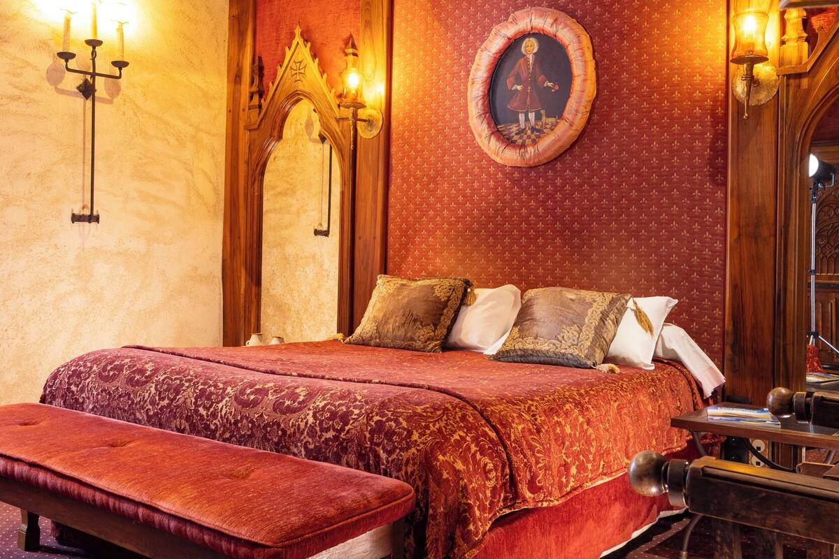 Una habitación con una cama grande, una banca, techo de madera y luces fijadas a la pared.