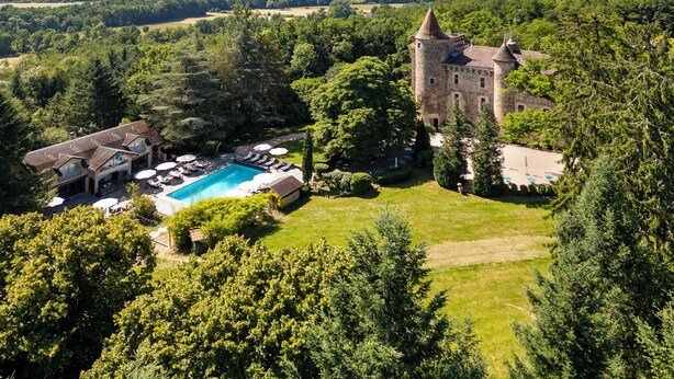 A castle with a swimming pool surrounded by lush greenery and a view of distant hills. - Château de Codignat (Bort-l'Étang)