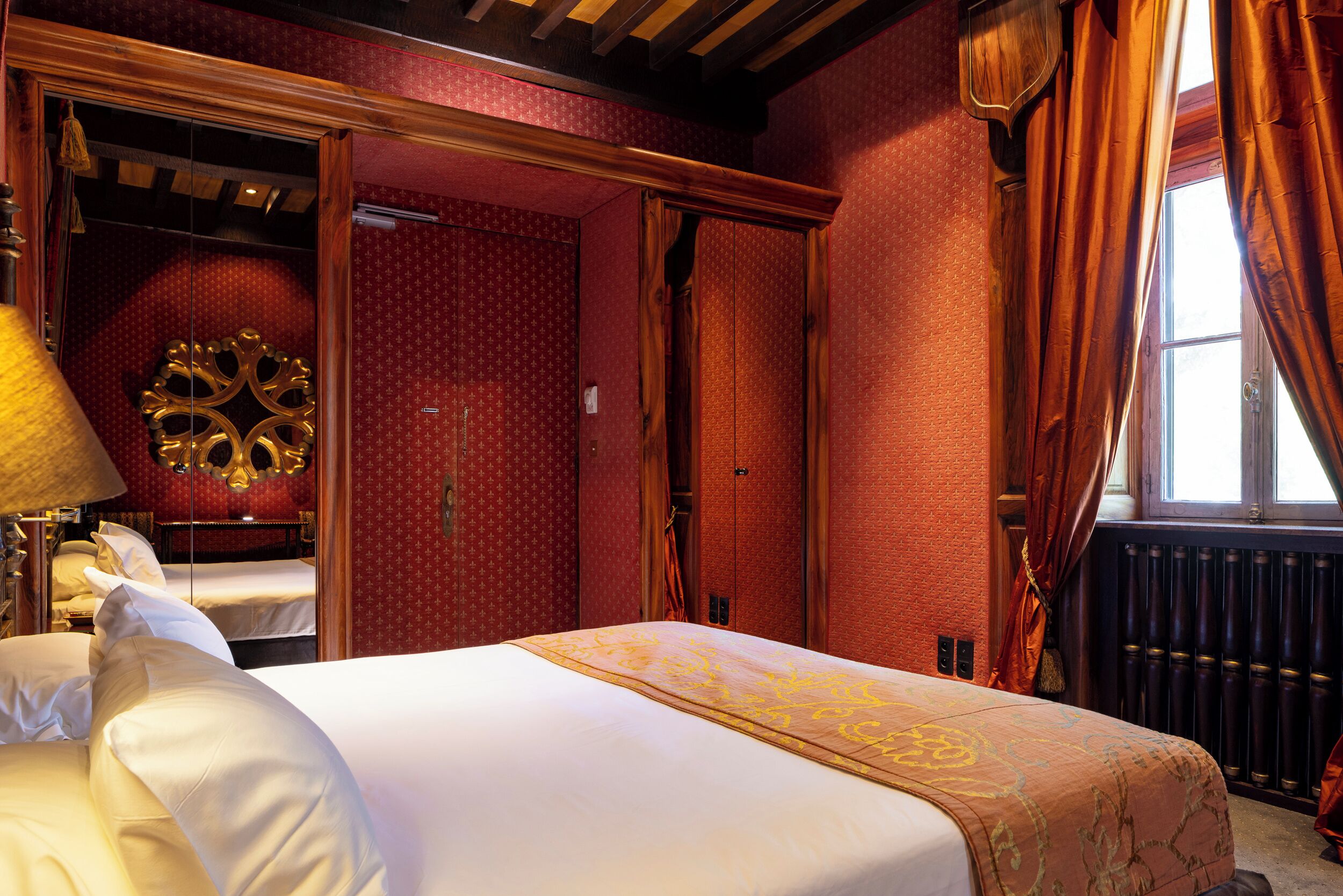 A hotel room with a large bed, a wooden ceiling, and a red patterned wall.