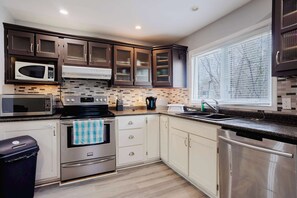 A modern kitchen with stainless steel appliances, white cabinetry, and a window with blinds.