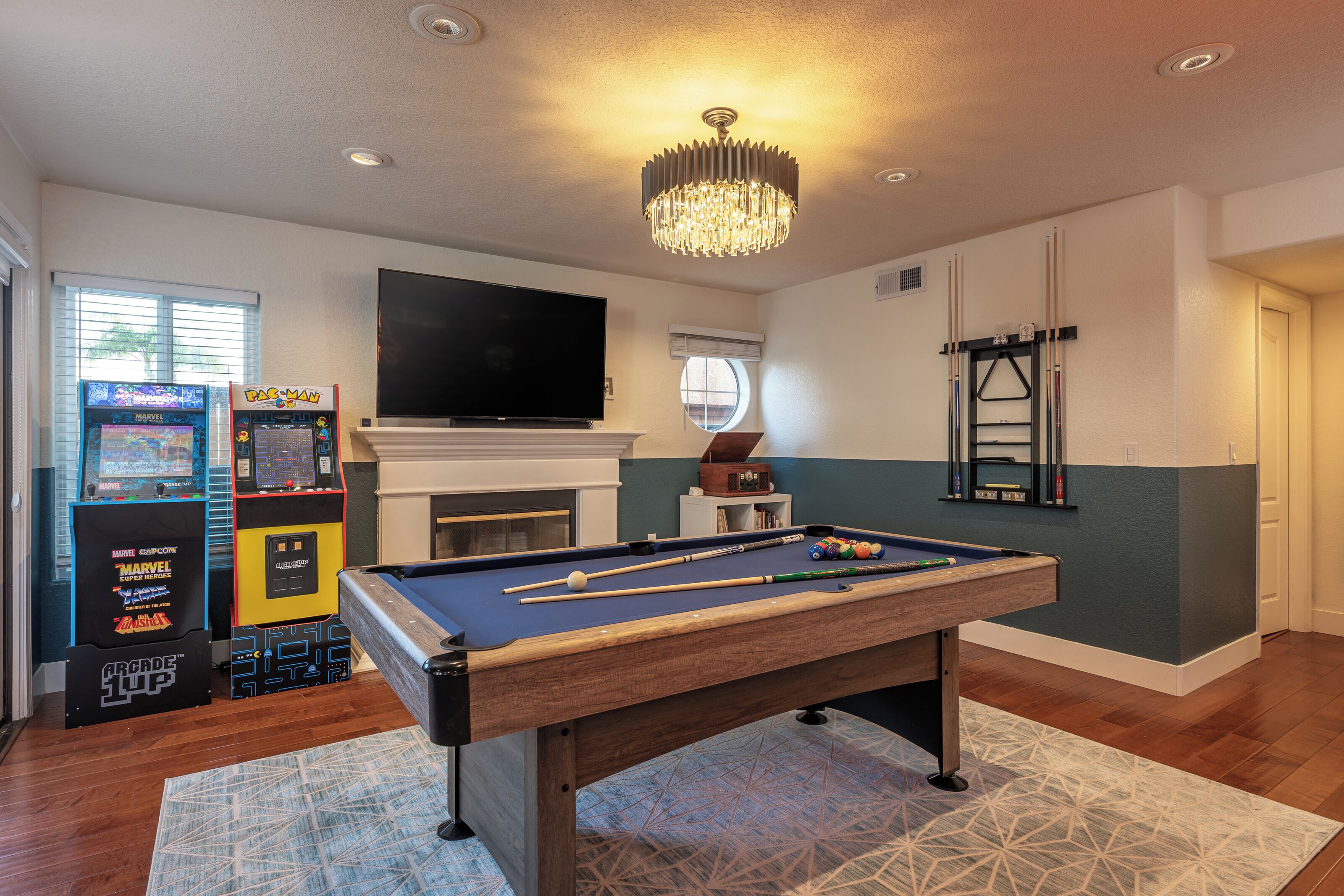 A room with a pool table, a flat-screen TV, arcade games, and a fireplace.