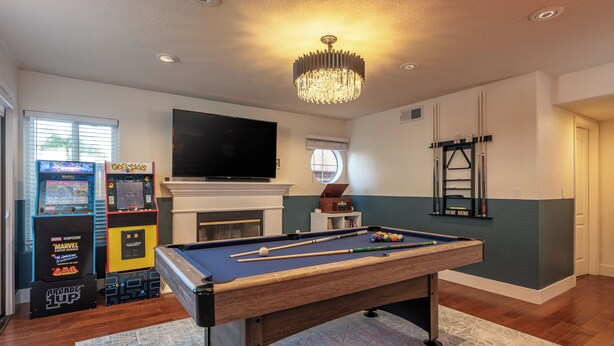 Una habitación con mesa de billar, juegos de arcade, televisor de pantalla plana y chimenea.
