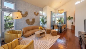 Un salon moderne avec un canapé d’angle, des fauteuils jaunes, une table basse ornée d’un vase de tournesols, un tapis à motifs et un coin repas agrémenté d’un lustre.