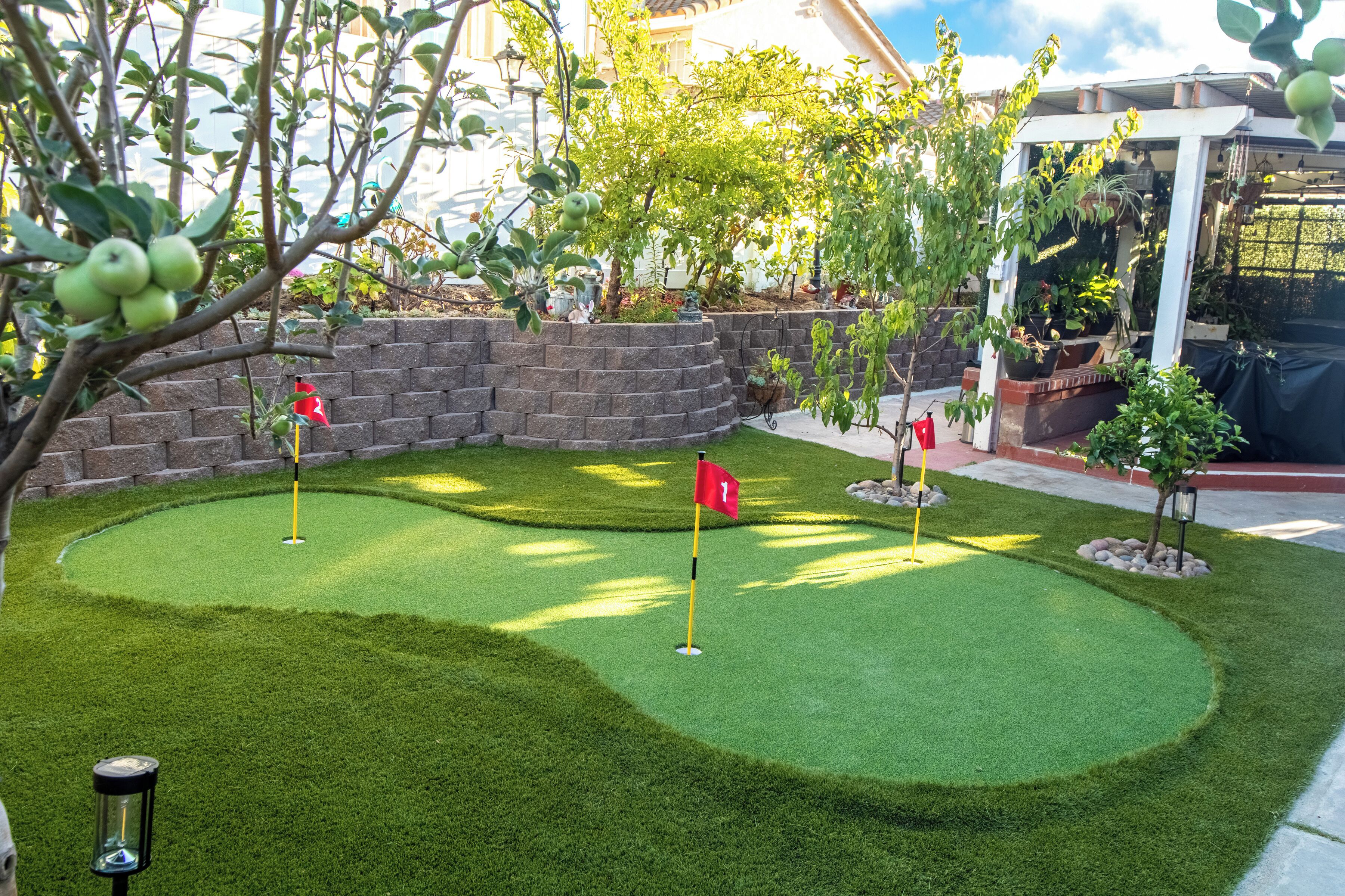 A miniature golf course with a well-maintained lawn, a brick wall, and various plants.