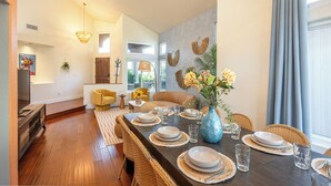 Un coin repas avec une longue table dressée pour quatre personnes, entourée de chaises en osier.