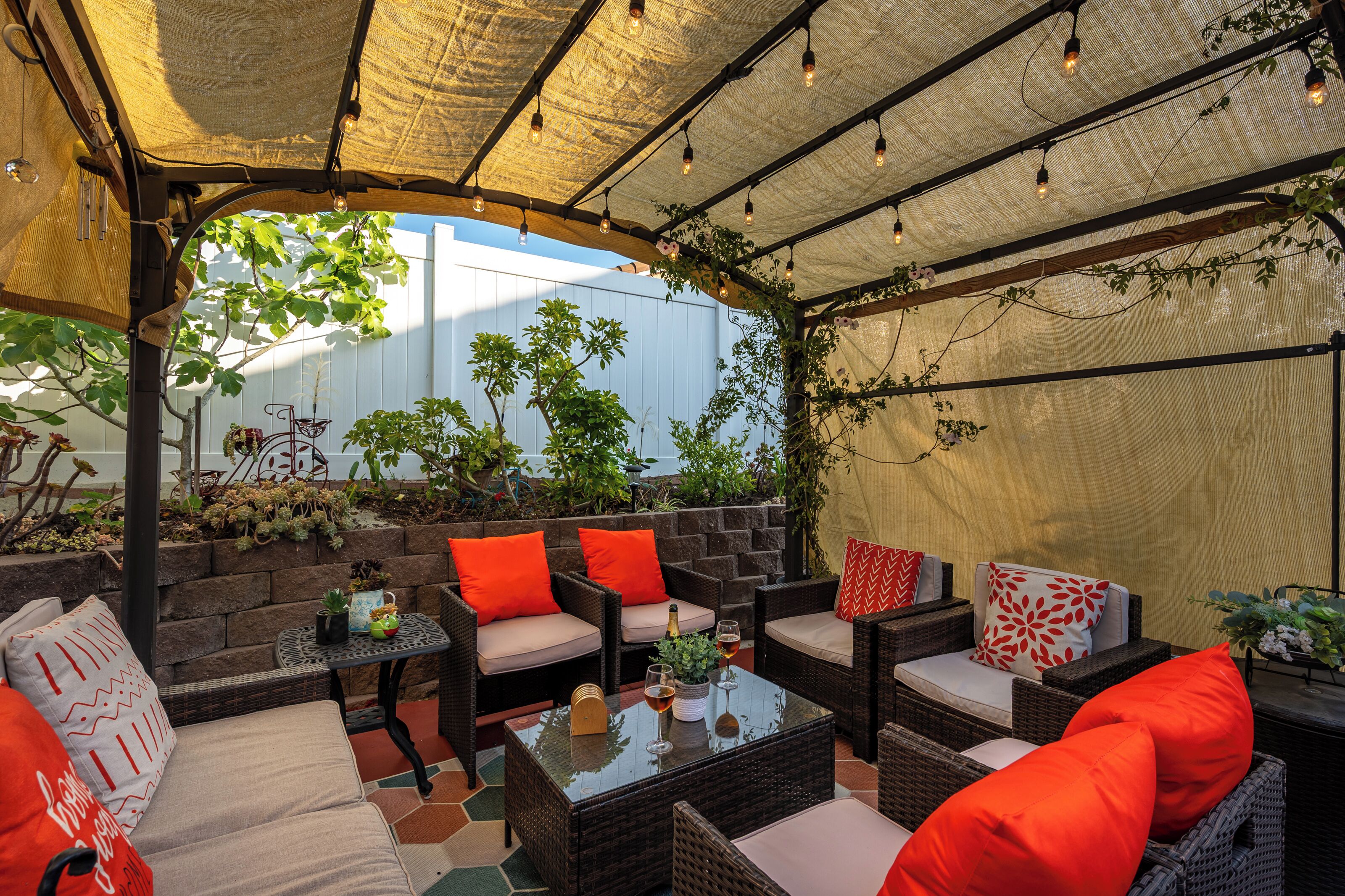 Une terrasse extérieure avec des meubles en osier, des coussins rouges et une table en verre.