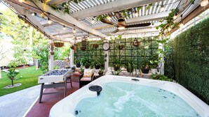 Un bain à remous surmonté d’une pergola, entouré de plantes en pot et agrémenté d’une table de baby-foot.