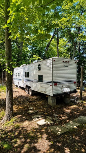 Un camping-car de la marque Fleetwood est garé dans une zone boisée, sous un ciel dégagé.