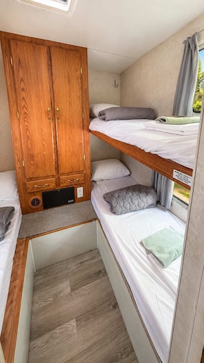 A compact RV interior with a bunk bed, a wooden wardrobe, and a small kitchenette.