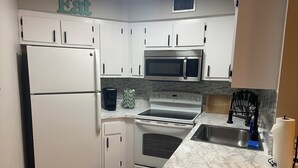 A kitchen with white cabinets, a refrigerator, a microwave, an oven, and a marble countertop.