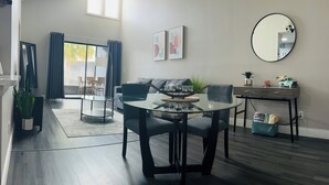 A modern living room with a glass dining table, grey sofas, and a large mirror.