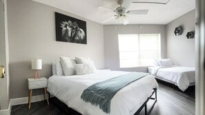 A bedroom with a large bed, a bedside table with a lamp, a ceiling fan, and a window with blinds.
