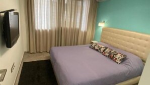Una habitación de hotel con cama, televisión, ventana con cortinas y aire acondicionado de pared.