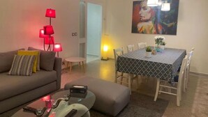 Una sala de estar con un sofá, una mesa de centro, una mesa de comedor con sillas y un cuadro en la pared.