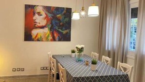 Un comedor con una mesa preparada para cuatro personas, un cuadro en la pared y una ventana con cortinas.