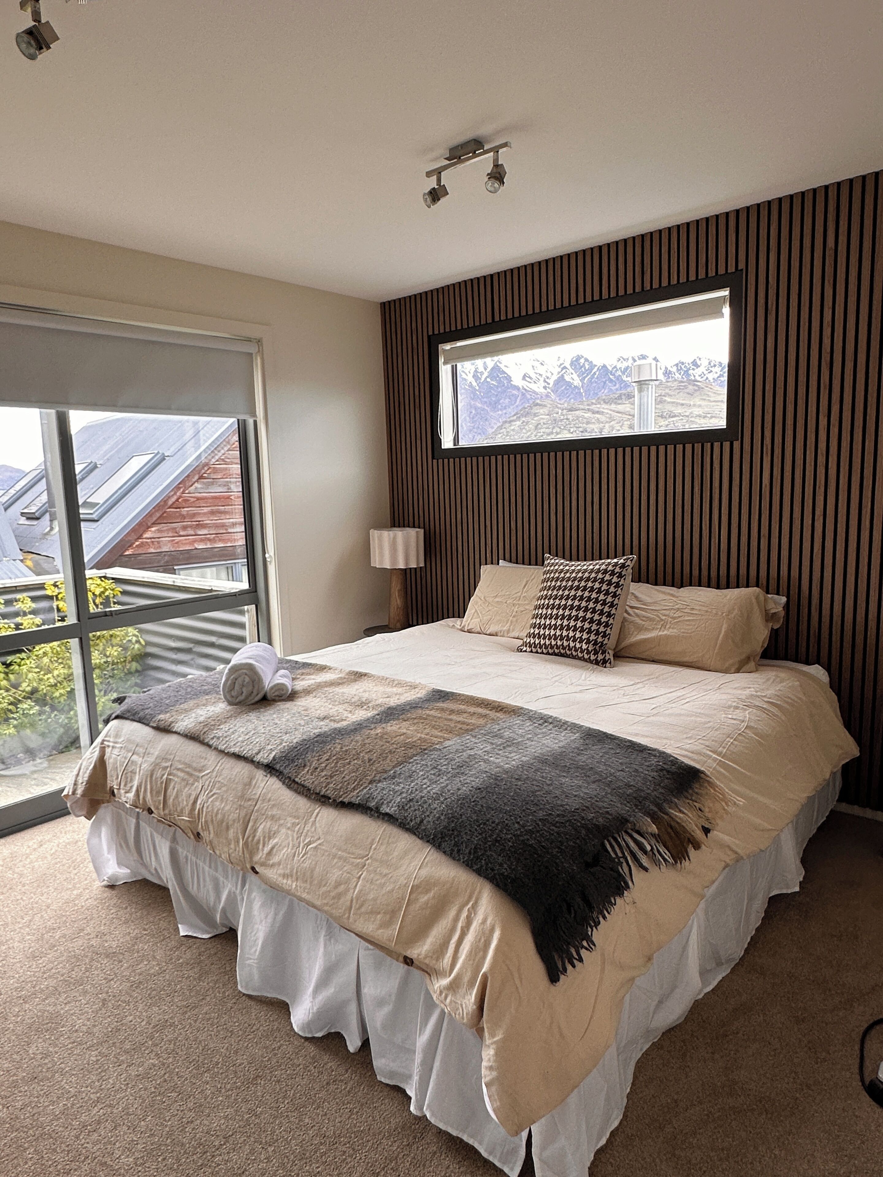 A bedroom with a large bed, a window with a view of mountains, and a ceiling light fixture.