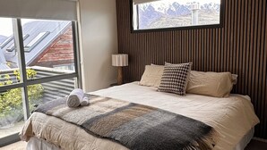 Une chambre avec un grand lit, une fenêtre donnant sur les montagnes et un luminaire au plafond.