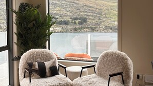Une pièce dotée d’une grande fenêtre donnant sur les montagnes, de deux fauteuils moelleux, d’une petite table et d’un luminaire suspendu.