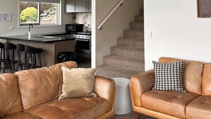 Un salon moderne avec des canapés en cuir, une table basse et un escalier menant à une cuisine dotée d’un coin bar.