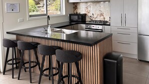 Une cuisine moderne dotée d’un îlot central, de tabourets de bar, d’appareils électroménagers en acier inoxydable et offrant une vue sur la verdure environnante.