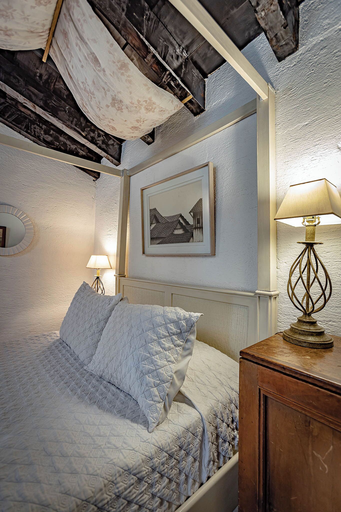 Ein Schlafzimmer mit einem Bett, einer Nachttischlampe, einem gerahmten Bild an der Wand und einem hölzernen Nachttisch.