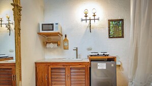 A bathroom with wooden cabinets, a sink, a mirror, a microwave, a bottle of alcohol, a small framed picture, and a shower curtain.