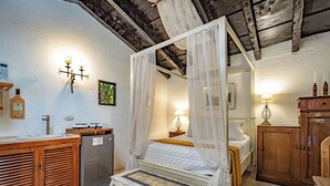 A bedroom with a canopy bed, a small refrigerator, wooden cabinets, and a bedside table with a lamp.