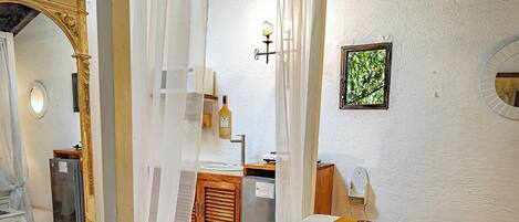 A four-poster bed with a canopy, a bedside table, a nightstand, and a small window with a view of greenery.