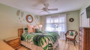 A bedroom with a bed, a chair, a dresser, a ceiling fan, and a window with curtains. - Coconut Cove: ACROSS from beach + boardwalk + parking w/ Full Linen Service! (Ocean City)