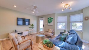 A modern living room with a sofa, chairs, a TV, and a ceiling fan. - Coconut Cove: ACROSS from beach + boardwalk + parking w/ Full Linen Service! (Ocean City)
