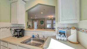 A kitchen with a stainless steel sink, a coffee maker, and a countertop with a basket and a welcome sign. - Coconut Cove: ACROSS from beach + boardwalk + parking w/ Full Linen Service! (Ocean City)