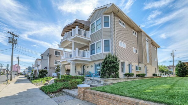 A multi-story residential building with a balcony, a well-maintained lawn, and a clear sky. - Coconut Cove: ACROSS from beach + boardwalk + parking w/ Full Linen Service! (Ocean City)
