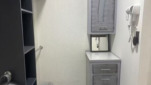 Casa de banho compacta com um armário cinzento, uma pia pequena e um secador de cabelo na parede.