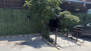 Uma área de estacionamento com grades de metal, uma árvore e um muro de pedra.