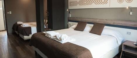 Habitación de hotel con una cama grande, una cama más pequeña, una mesita de noche de madera y una obra de arte colgada en la pared.