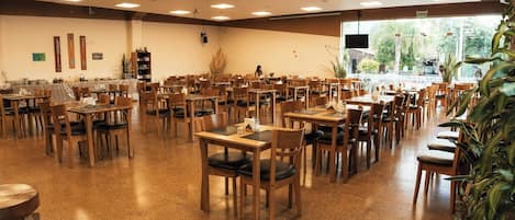 A spacious dining area with multiple tables and chairs, a buffet setup, and a large window providing a view of the outdoors.