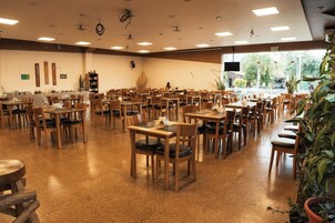 Un comedor amplio con varias mesas y sillas, un sistema de buffet y un gran ventanal con vistas al exterior.