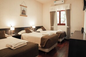 Quarto de hotel com três camas, uma escrivaninha e uma janela com cortinas.
