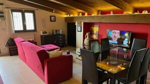 A living room with a red sofa, a glass dining table with chairs, a television, and a fireplace. - MODERN APARTMENT SURROUNDED BY GREENERY BUT A STONE'S THROW FROM THE SEA AND MOUNTAINS (Lazio)