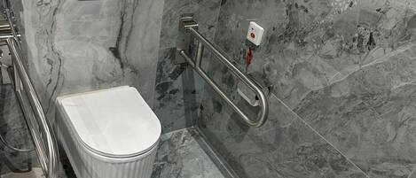 A bathroom with a white toilet, a white sink, and a shower area with a handrail.