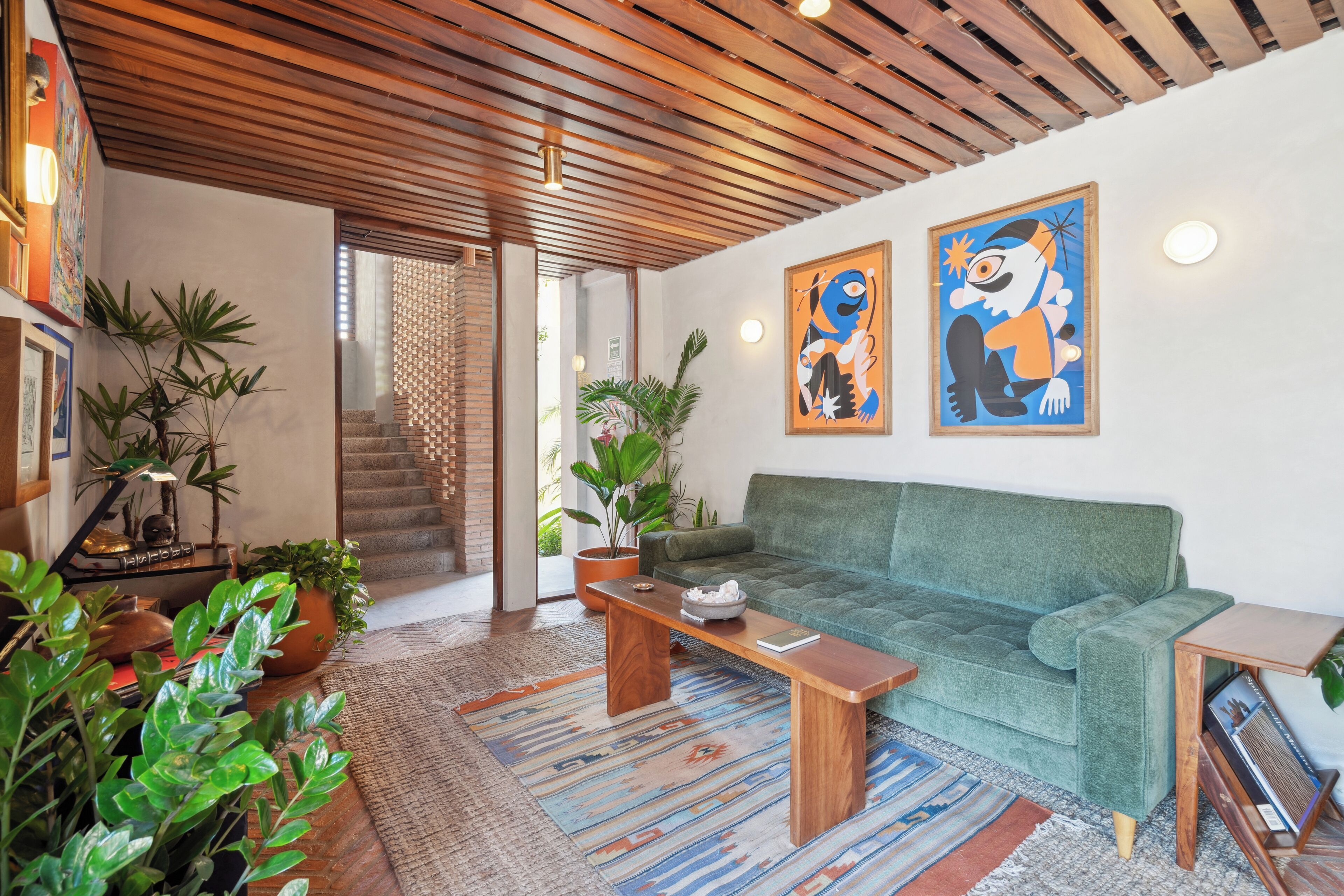 Una sala de estar moderna con un sofá verde, una mesa de centro de madera y diversas plantas.