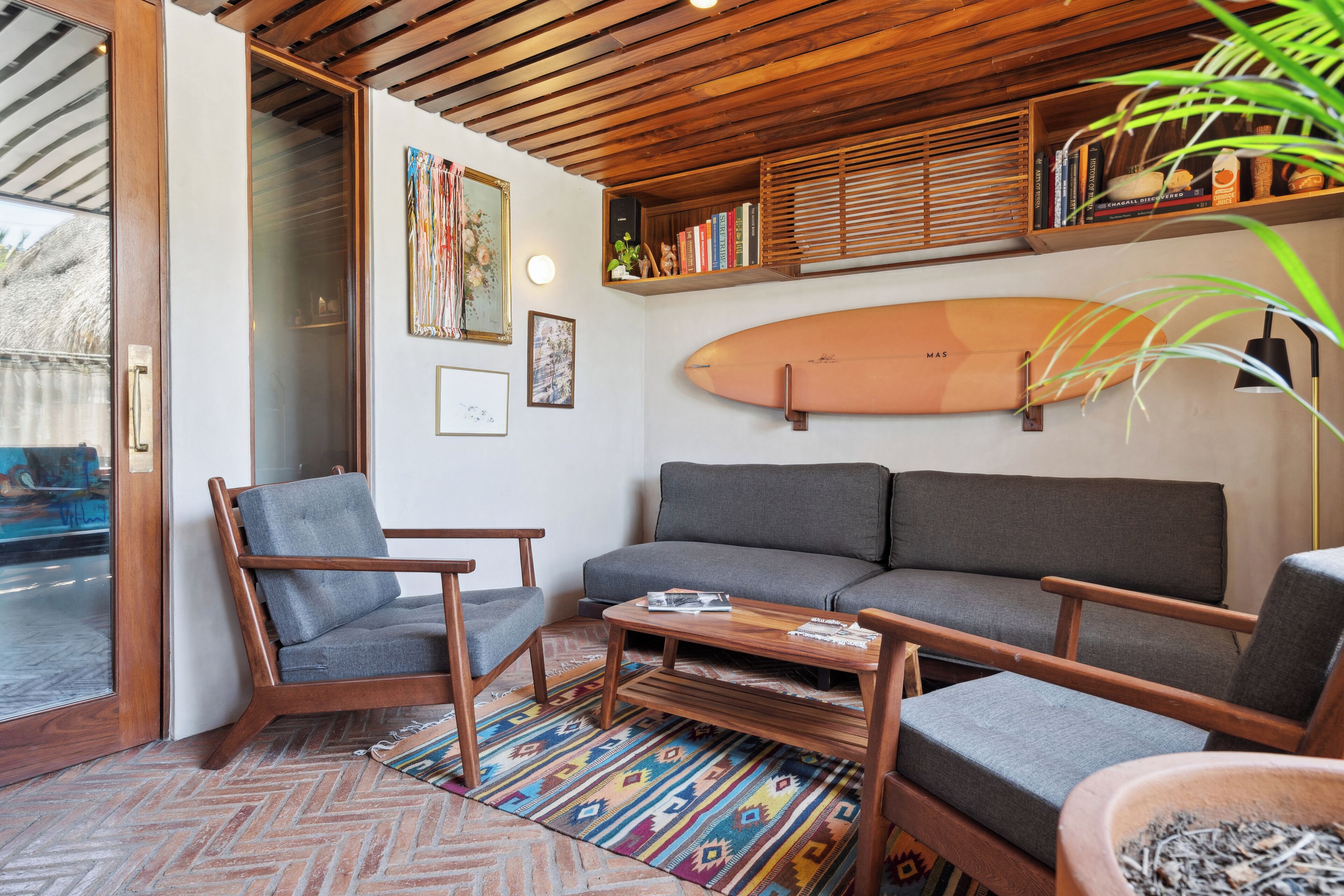 Un salon confortable avec un canapé, des fauteuils, une table basse et une planche de surf accrochée au mur.