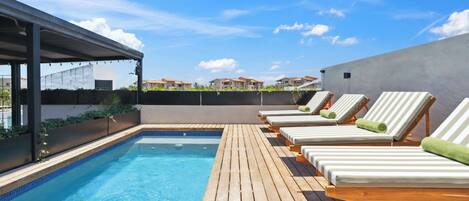 A rooftop pool area with lounge chairs and a covered seating area.