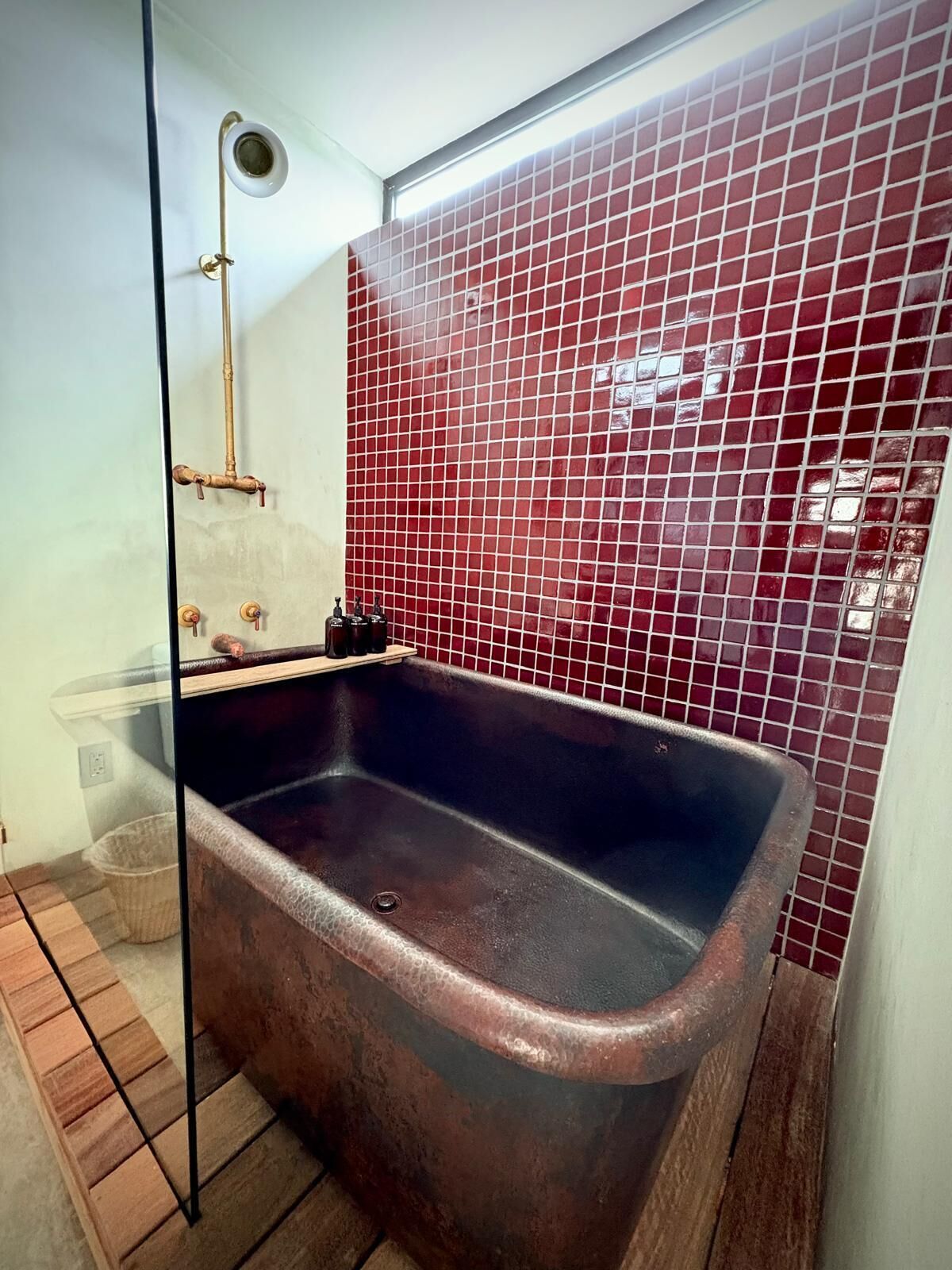 A bathroom with a freestanding bathtub, a glass shower enclosure, and red-tiled walls.
