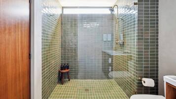 Ein Duschbereich mit grünen Fliesen an Wänden und Boden, einer Holztür sowie einer Toilette mit weißem Deckel.