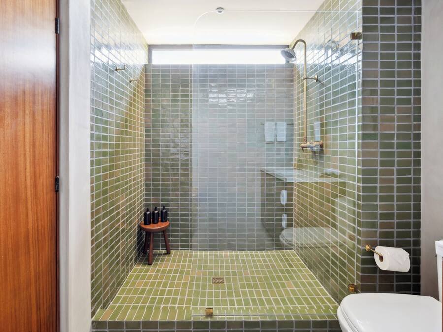 Ein Duschbereich mit grünen Fliesen an Wänden und Boden, einer Holztür sowie einer Toilette mit weißem Deckel.