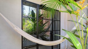 A hammock tied between two windows, a brick wall, and a potted plant. - ALMA Surf Lodge (Punta de Mita)